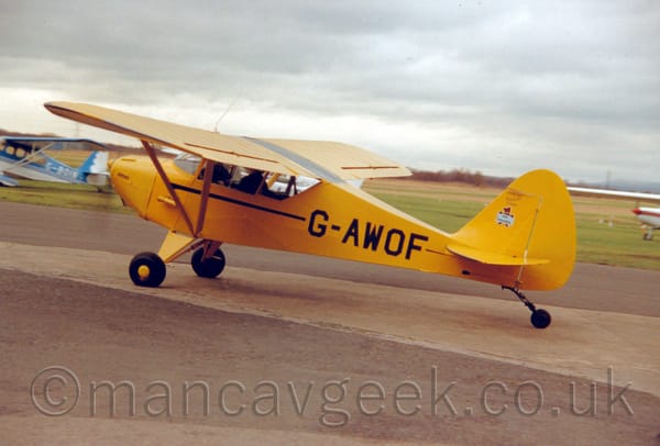 Side view of a high-winged, single engined light aircraft taxiing from right to left.