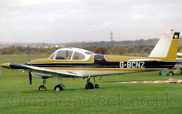 Side view of a single engined, green and white light aircraft parked facing to the left on grass.