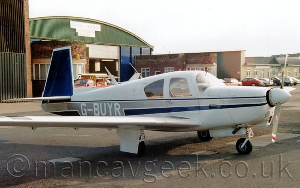 Side view of a single engined light aircraft parked on black tarmac facing to the right.
