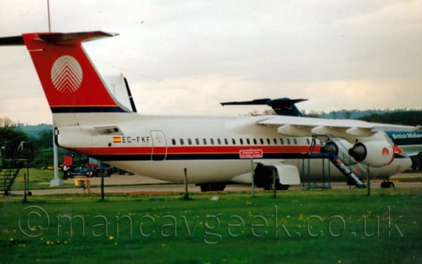 Side view of a white and red, high-winged, 4 engined jet airliner parked facing to the right.