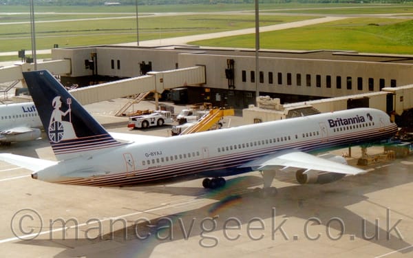 Slightly elevated side view of a blue and white, twin engined jet airliner parked on it's gate, facing to the right.