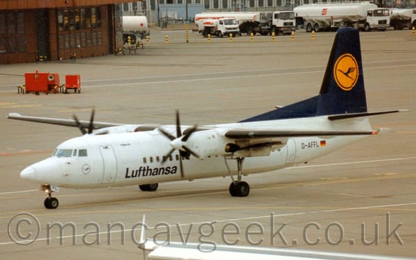 Side view of a white, high-winged, twin propellor-engined airliner taxiing from right to left.