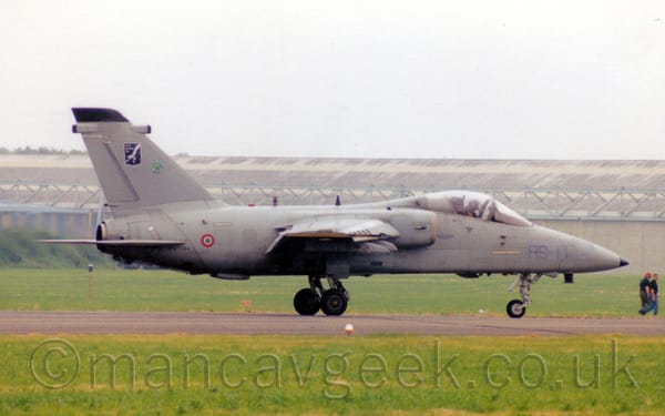 Side view of a grey, single-engined military jet fighter aircraft taxiing from left to right along a black runway.