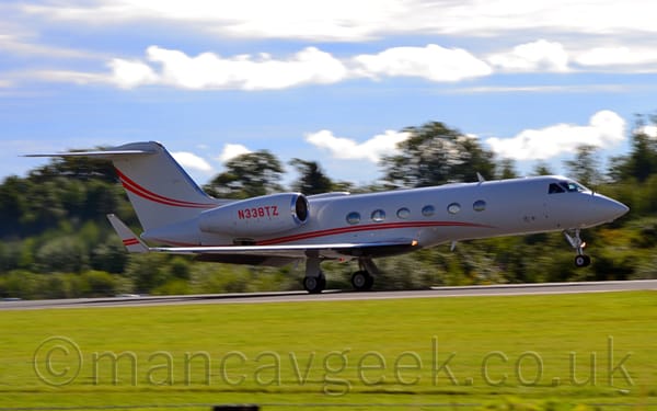 Side view of a white, twin engined BizJet moving at speed from left to right, flaps extended from behind the wings, and the nose raised, suggesting it is either taking off or landing.