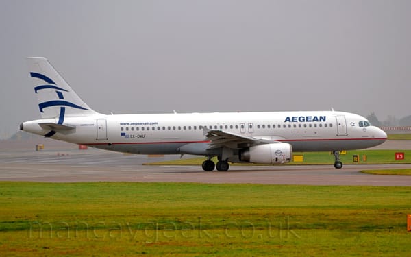 Side view of a twin engined jet airliner taxiing from left to right. The plane is mostly white, with a grey belly and a red pin-stripe.