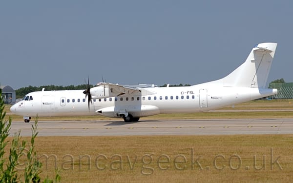 Side view of a white, high-winged, twin propellor-engined airliner taxiing from right to left along a grey runway.