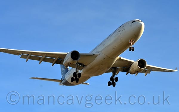 Low view of a white twin-engined jet airliner flying from left to right at a very low altitude