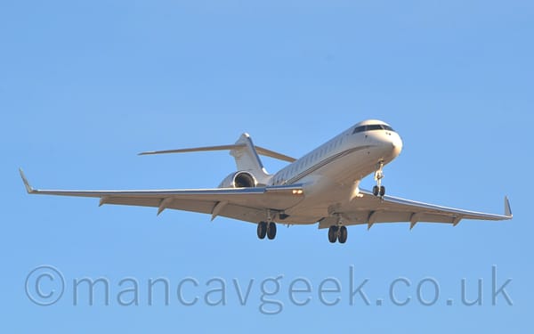 Low 3/4 view of a white, twin engined BizJet with the engines mounted on the sides of the rear fuselage, flying from left to right at a very low altitude