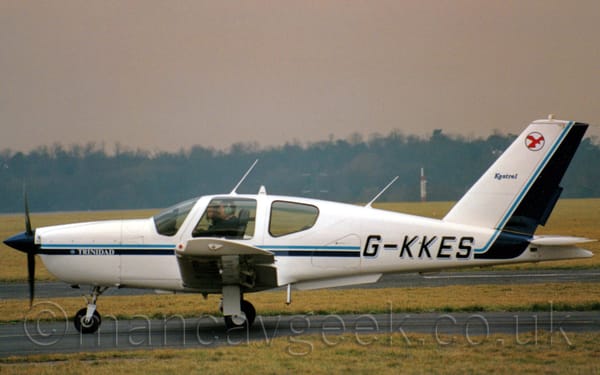 Side view of a single-engined light aircraft taxiing from right to left along a black taxiway.