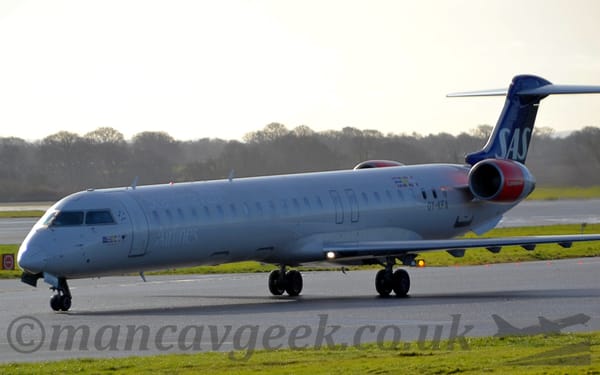 Side view of a twin engined jet airliner with the engines mounted on the sides of the rear fuselage, taxiing from right to left.