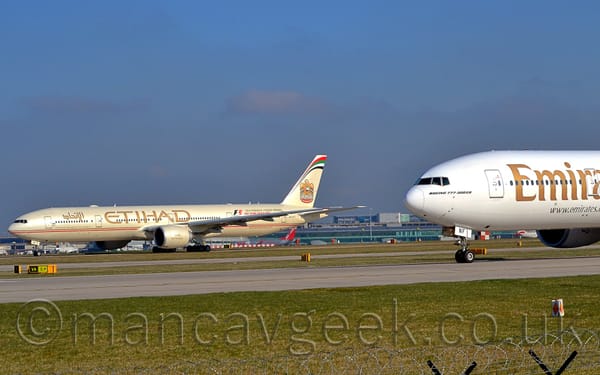 A side view of a pair of twin engined jet airliners parked facing to the right.