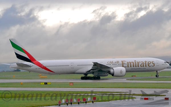 Side view of a large twin engined jet airliner taxiing from left to right along a grey taxiway.