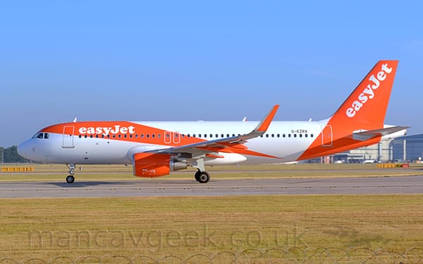 Side view of a twin engined jet airliner parked facing to the left on a grey runway.