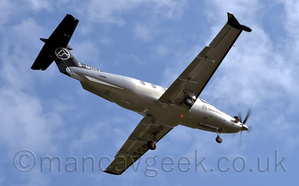 Low side view of a single-engined BizProp flying from left to right, almost directly overhead, at a very low altitude.