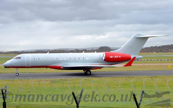 Side view of a grey, twin engined BizJet taxiing from right to left.