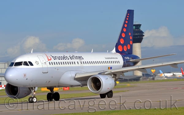 Side view of a twin engined jet airliner taxiing from right to left, turning onto a grey runway.