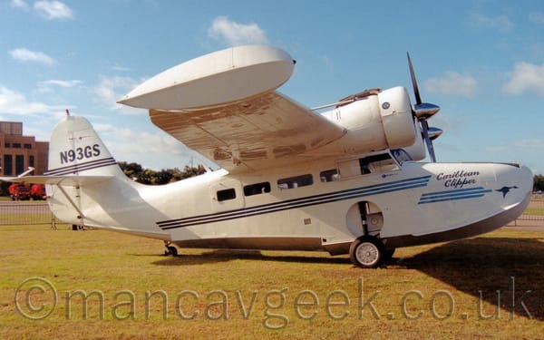 Side view of a white, twin propellor-engined amphibious plane parked on grass, facing to the right.