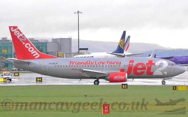 Side view of a grey and red, twin engined jet airliner taxiing from left to right.