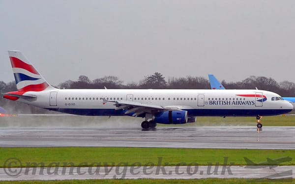 Side view of a twin engined jet airliner moving rapidly from left to right on a slightly damp runway.