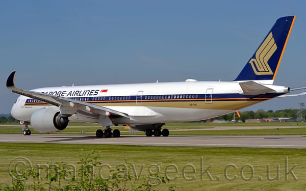 Rear side view of a twin engined jet airliner moving from right to left along a dark grey runway.