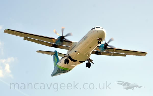 Low front view of a high-winged, twin propellor-engined airliner flying from left to right at a very low altitude