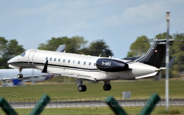 Side view of a twin engined jet airliner flying from right to left at a very low altitude, just a couple of metres above a runway