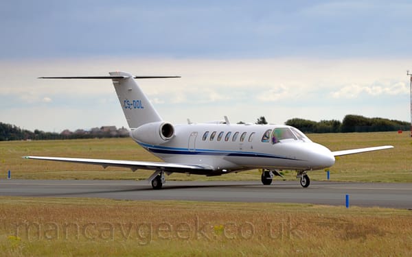 Side view of a twin engined white BizJet taxiing from left to right.