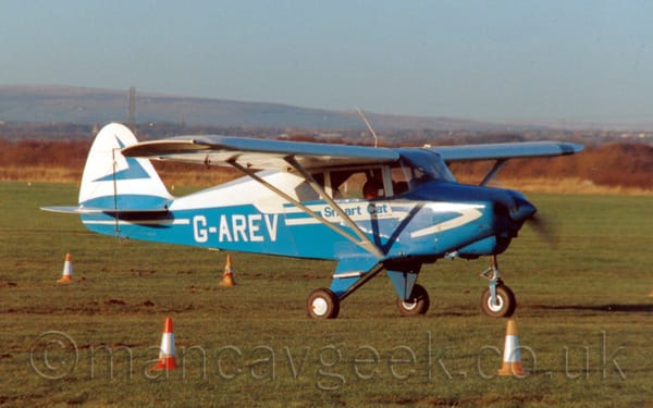 Side view of a high-winged, single engined light aircraft taxiing from left to right on grass.