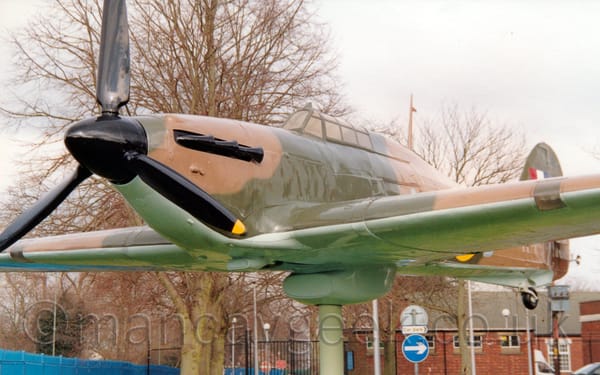 Low front view of a single engined, World War 2-era military fighter aircraft, mounted on a creamy green pole in a flying position.