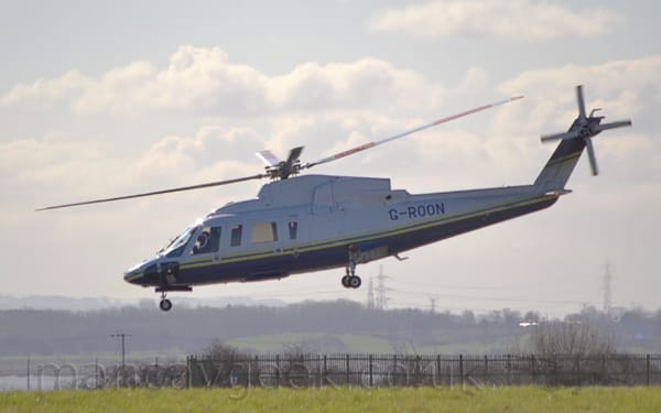 Side view of a helicopter flying from right to left at a low altitude with it's undercarriage extended.