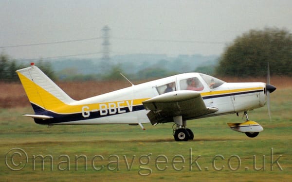 Side view of a single-engined light aircraft on a grass runway, moving from left to right