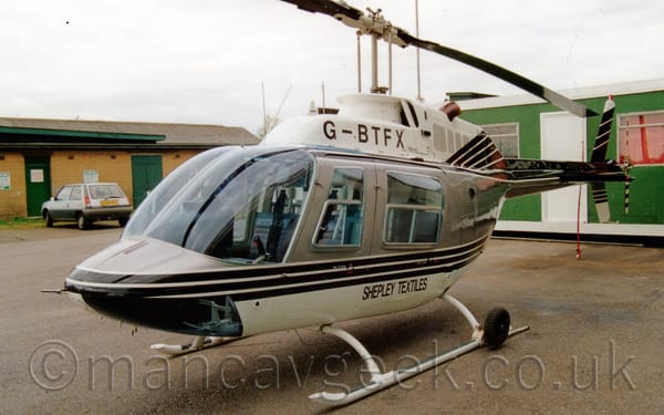 Side view of a white and grey helicopter parked on tarmac facing to the left.
