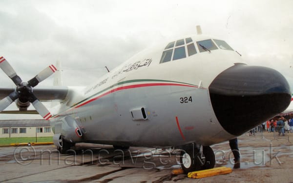 Front side view of the nose and forward fuselage of a high-winged, 4 propellor-engined military cargo plane parked facing to the right.
