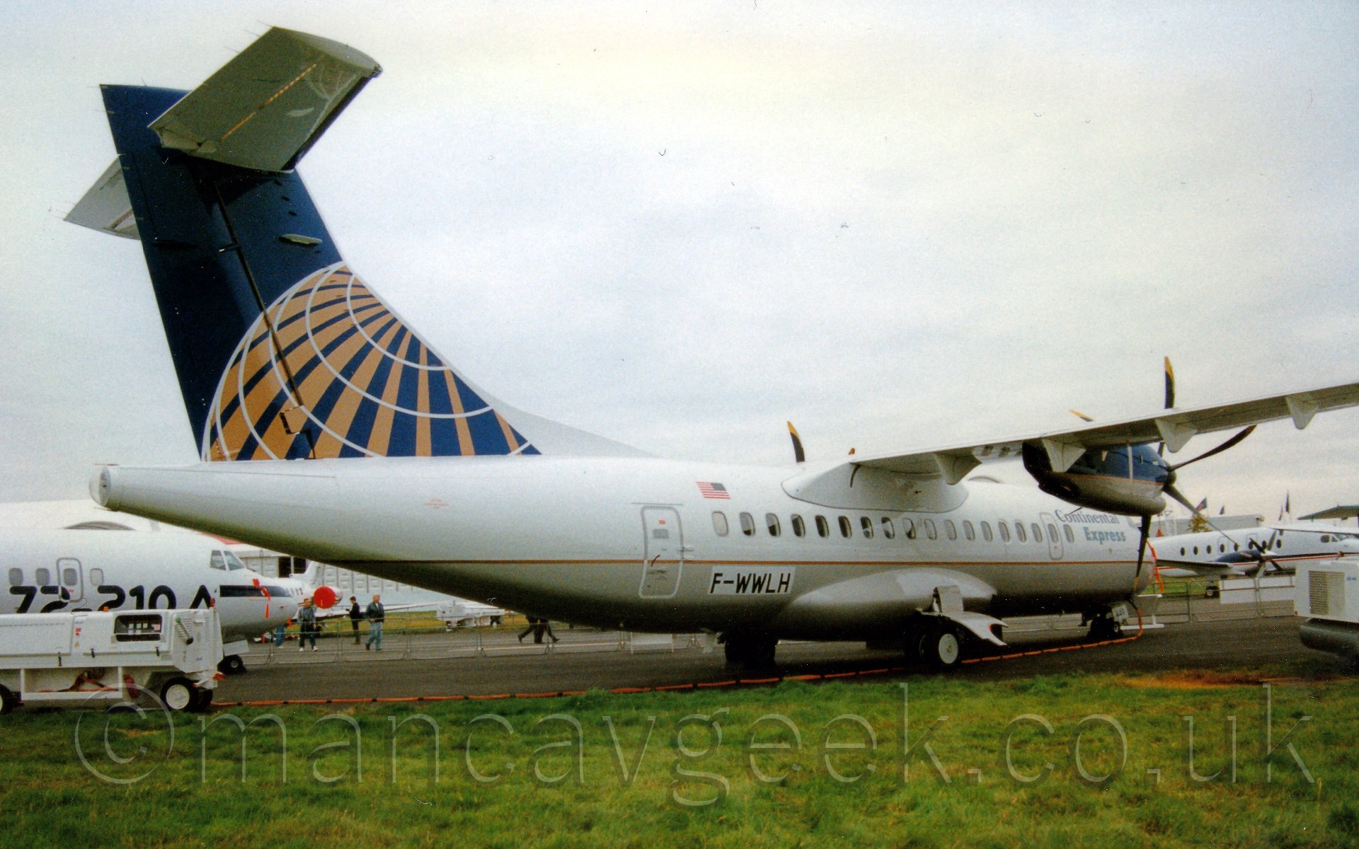 Side view of a high-winged, T-tailed twin propellor-engined airliner facing to the right and slightly away from the camera. The plane is mostly white, with a sandy brown belly, and a thin golden stripe, with blue "Continental Express". There is a white patch on the lower rear fuselage with the registration "F-WWLH". The tail is a deep blue, with a white and golden wireframe globe. Below the tail and behind the tail are other propellor airliners on static display, with occasional people walking around. Above it all, the sky is a flat grey.