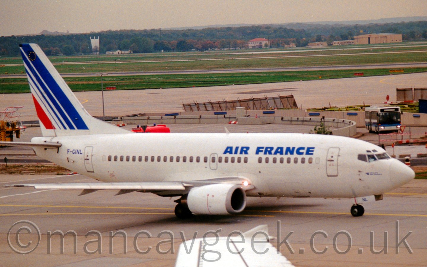 Side view of a twin engined white jet airliner with blue "Air France" titles on the upper forward fuselage and diagonal blue and red stripes on the tail taxiing from left to right.