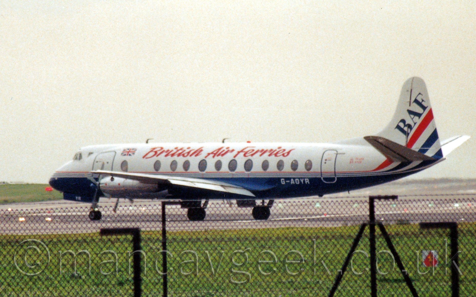 Side view of a white, 4 propellor engined airliner with a blue belly and red "British Air Ferries" titles on the upper fuselage, taxiing from right to left under a hazy but bright white sky.