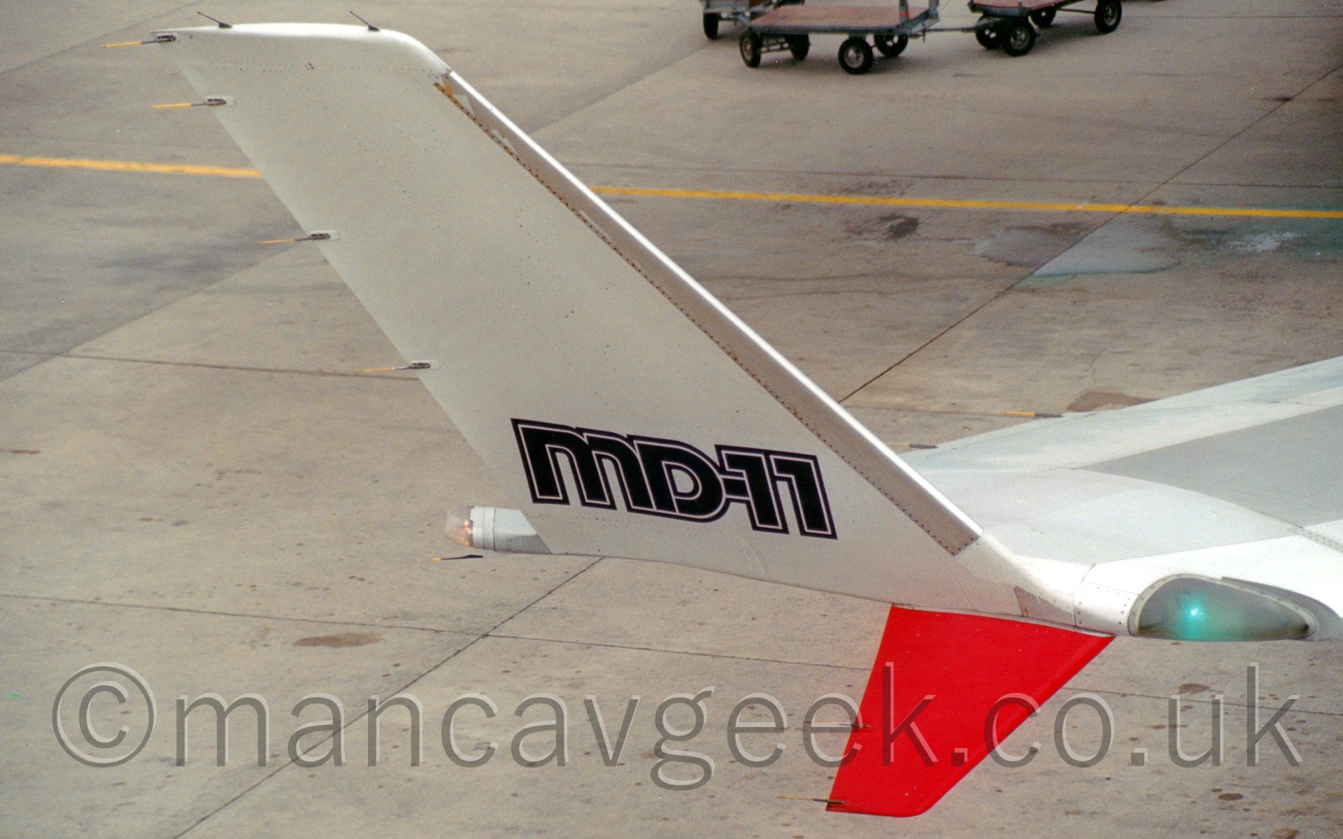 Closeup of the upturned wingtip of a jet airliner facing to the right, with black "MD-11" titles, a red downturned section, and a flashing green light at the front.