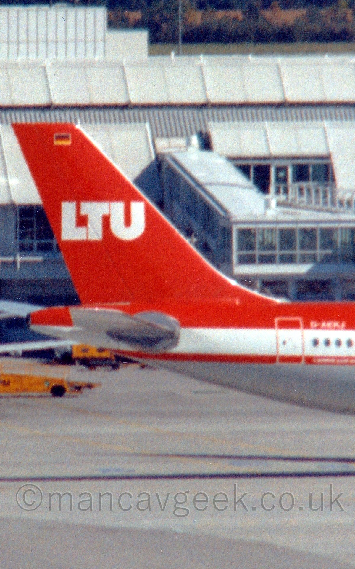 Close up of the red tail of a red, white, and grey jet airliner taxiing from left to right.