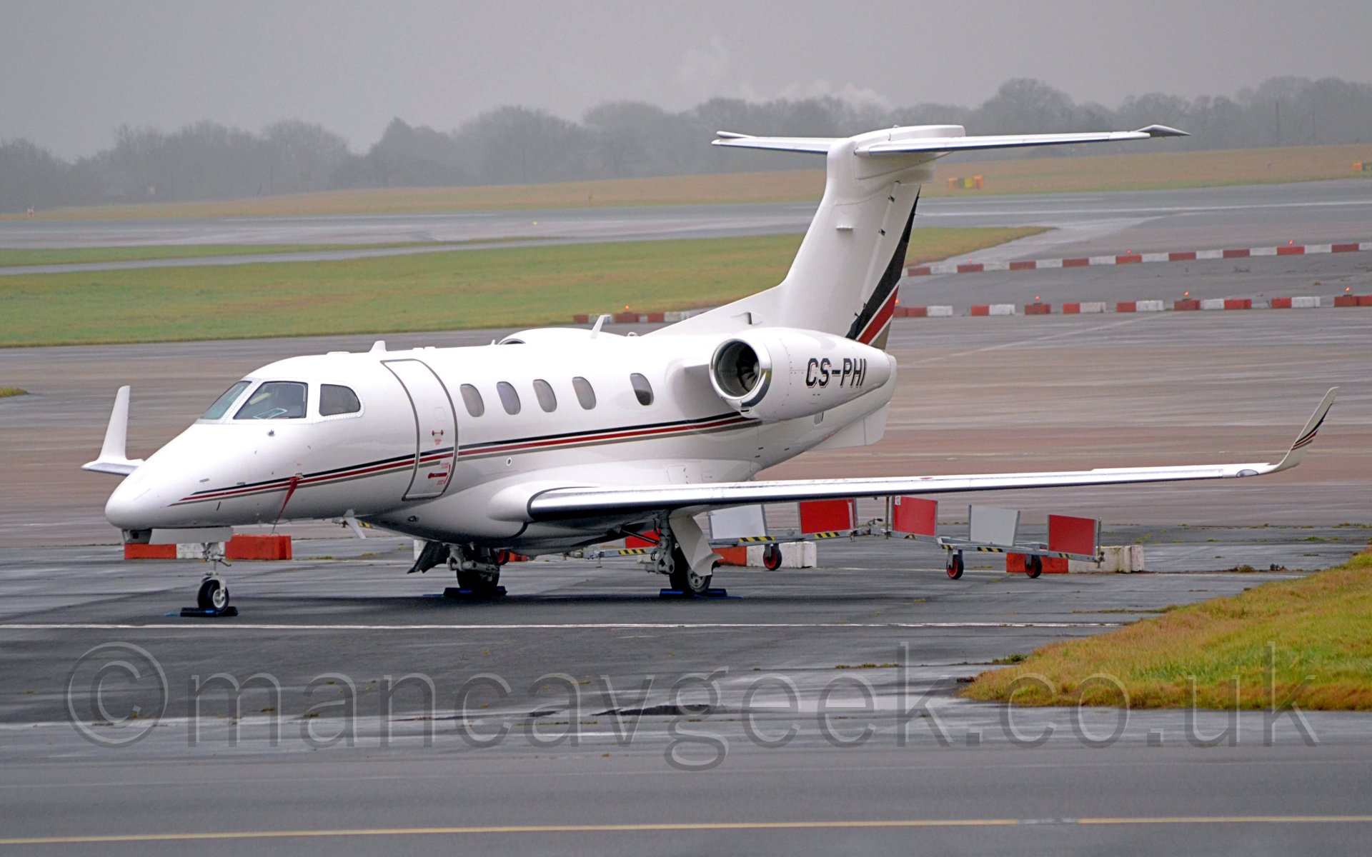 Side view of a white, twin engined bizjet parked facing to the left under a dismal grey sky.