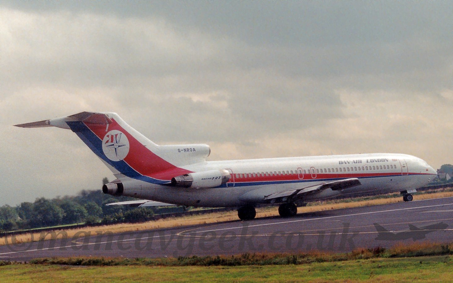 Side view of a white, red, and blue, 3 engined jet airliner with the engines mounted on the rear fuselage, turning on to the runway for take off, under ominous grey clouds.