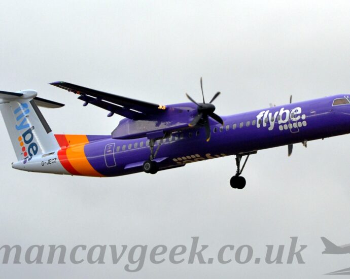 Low side view of a high-winged, twin propellor-engined airliner flying from left to right at a low altitude, with undercarriage lowered and flaps extended from the rear of the wings, suggesting it is about to land. The plane is almost entirely purple, with an orange and purple band around the rear fuselage, and a white tail-cone and tail. There are white., billboard-style "FlyBe" titles above 6 white dots on the side of the forward fuselage, with similar diagonal titles in light and dark blue on the tail, over 2 orange, 2 red, and 2 purple dots. The white titles are also inverted on the underside of the fuselage. The engine pods mounted out on the wings are also purple, with the main undercarriage hanging down on long, spindly legs from the rear. The black registration "G-JECZ" is on the side of the tail-cone right at the rear. Flat grey clouds fill the rest of the frame.