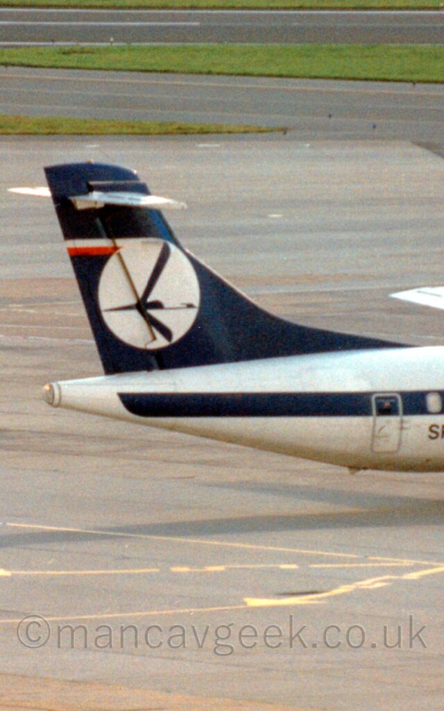 Close-up of the white rear fuselage and blue tail of a propellor-engined airliner taxing from left to right. The body of the plane is white, with a dark blue stripe running along the body. The tail is dark blue with a white circle with a stylised blue flying bird in the middle. Grey concrete apron fills the foreground, with more in the background with the occasional strip of grass breaking up the monotony.