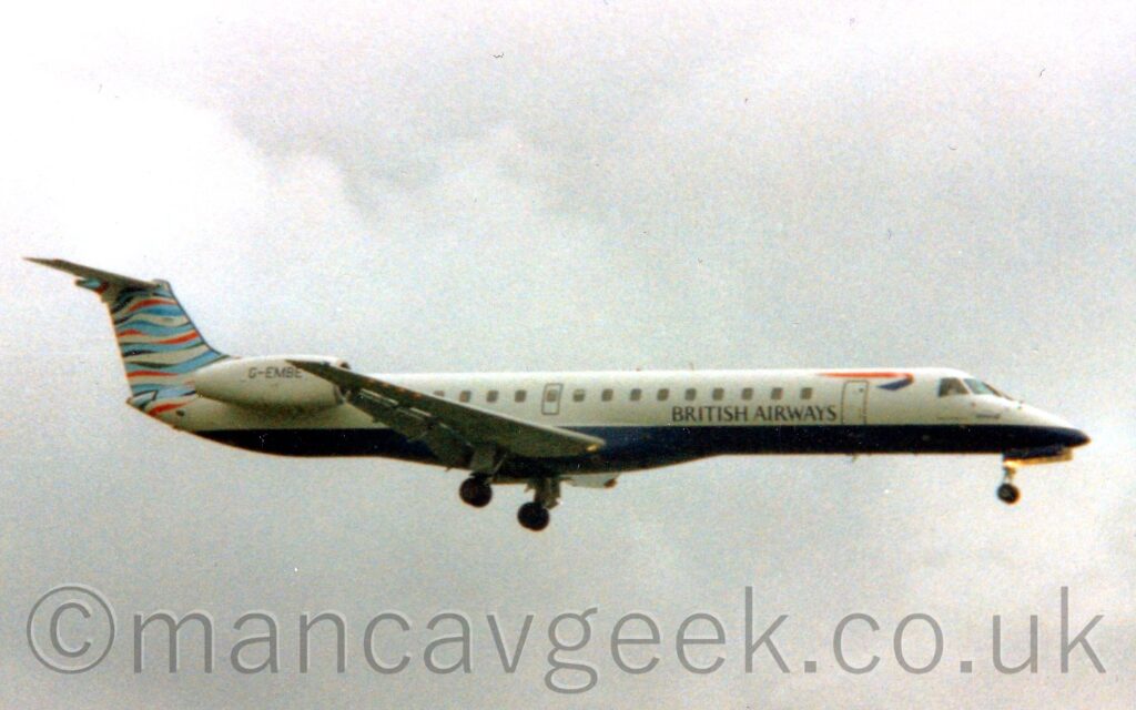 Side view of a white, twin engined jet airliner flying from left to right at a low altitude, with undercarriage lowered and flaps extended from the rear of the wings, suggesting it is about to land. The plane has a dark blue belly, with black "British Airways" on the lower forward fuselage, below a twisted red and blue ribbon. The tail has wavy light blue, dark blue, red, and white stripes. Cloudy grey sky fills the rest of the frame.