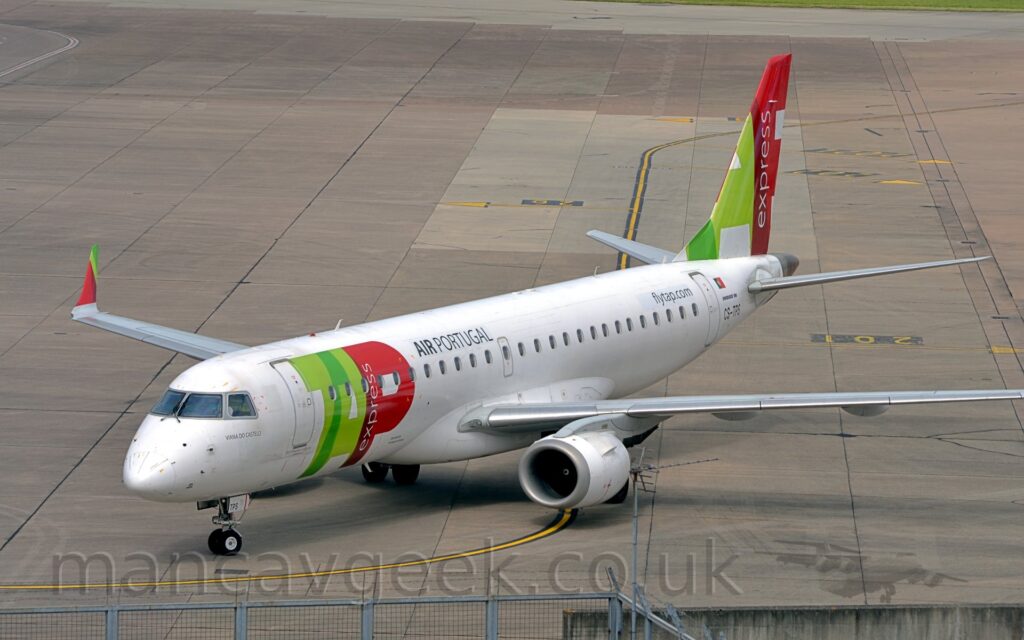 Slightly elevated side view of a twin-engined jet airliner taxiing from right to left. The plane is mostly white, with billboard-style, red and green "TAP" titles on the side of the forward fuselage, with smaller "Air Portugal " titles above the windows at the front of the passenger cabin. The tail has part of those same large red and green titles, with white "Express" titles arranged vertically in the long stroke of the red letter "P". Grey concrete apron marked with lines for planes to follow fills the rest of the frame.