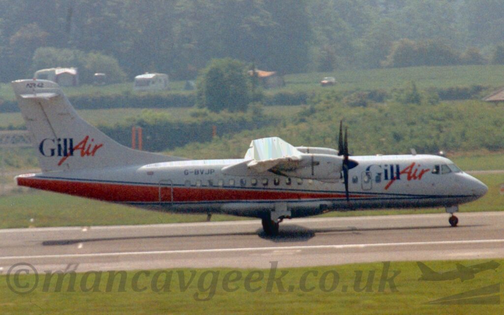 Side view of a high-winged, twin propellor-engined airliner accelerating from left to right along a grey runway. The plane is mostly white, with a red stripe outlined in blue coming from under the nose, slowly getting wider as it moves rearwards until it fills nearly all the rear fuselage. There are dark blue "Gill" titles on the upper forward fuselage, next to large, red, italic "Air" titles, a design replicated in a slightly smaller form on the white tail. The black registration "G-BVJP" is on the upper rear fuselage. Green grass fills the foreground, lining the side of the runway. In the background, more grass on the other side of the runway leads up to trees and bushes in the distance.
