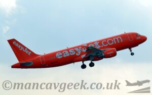 Side view of a bright orange, twin engined jet airliner flying from left to right at a low altitude, with undercarriage still lowered, flaps slightly extended from the rear of the wings, and the nose raised sharply, suggesting it has just taken off. There are large, white "EasyJet.com" titles written across the fuselage, with smaller "EasyJet" titles on the engine pods under the wings, as well as diagonally on the tail. There is a large white number "200" on the forward fuselage just under the cockpit windows, and the black registration "G-EZUI" on the lower rear fuselage. Pale blue sky with white patches of cloud fill the rest of the frame.