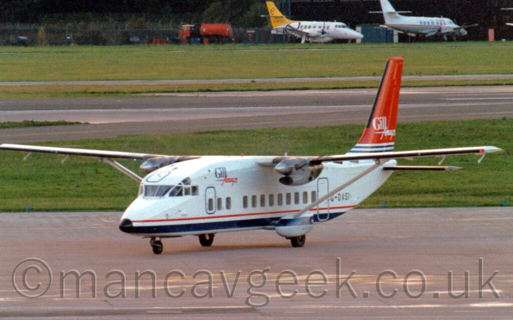 Front side view of a rather boxy-looking, high-winged, twin propellor-engined airliner taxiing from right to left. The plane is mostly white, with a thin red pinstripe and a thicker blue stripe running along the bottom of the body, and the black registration "G-DASI" on the side of the rear fuselage. There are a couple of words printed on the side of the upper forward fuselage - "Gill", in blue, with "Airways" in red pretty much underneath it, looking slightly hand drawn. The tail has a couple of thin dark blue stripes on the bottom, with the rest being a flat red, with the white words "Gill Airways" towards the middle. Grey apron fills the foreground, with a couple of large grassed areas and a wide, black runway filling most of the background, with a pair of small, white, twin propellor-engined airliners parked against trees on the far side.