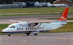 Side view of a squat and boxy, high-winged, twin propellor-engined airline taxiing from right to left. The plane is largely white, with a thin red and thicker blue stripe running along the bottom of the body, and blue and red "Gill Airways" titles on the upper forward fuselage, as well as the black registration "G-DASI" on the lower rear, just aft of the main pasenger door. The tail is red, with thin blue and white stripes at the bottom, and white "Gir Airways" titles in the middle. White sponsons with a blue stripe at the top stick out from the bottom of the fuselage, covering the main landing gear, with support struts extending p and out to support the outer sections of the very thin wings. Grey concrete apron fills the foreground, with grass and a black runway in the background. grey prefabricated buildings can be seen in the top left corner, with a white, twin engined BizJet in the top right corner.